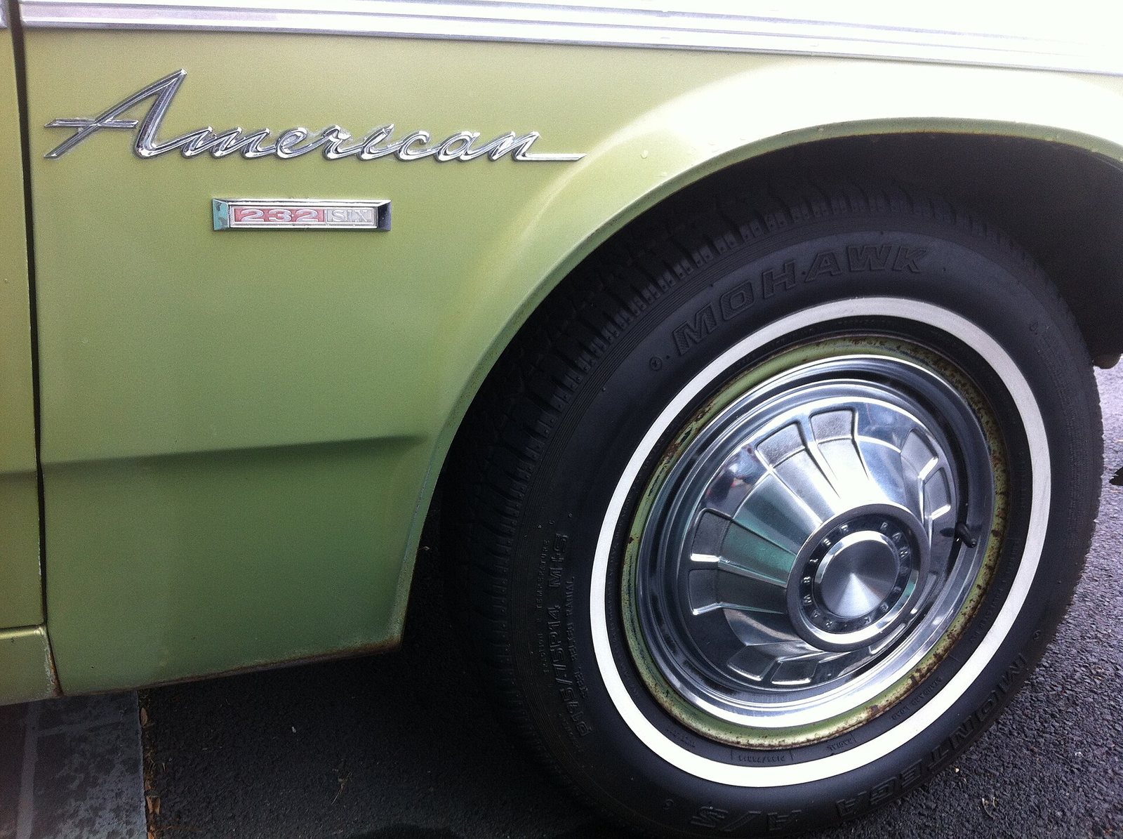 Aleta delantera de un Rambler American de 1968 con su emblema, la rueda de banda blanca y el tapacubos