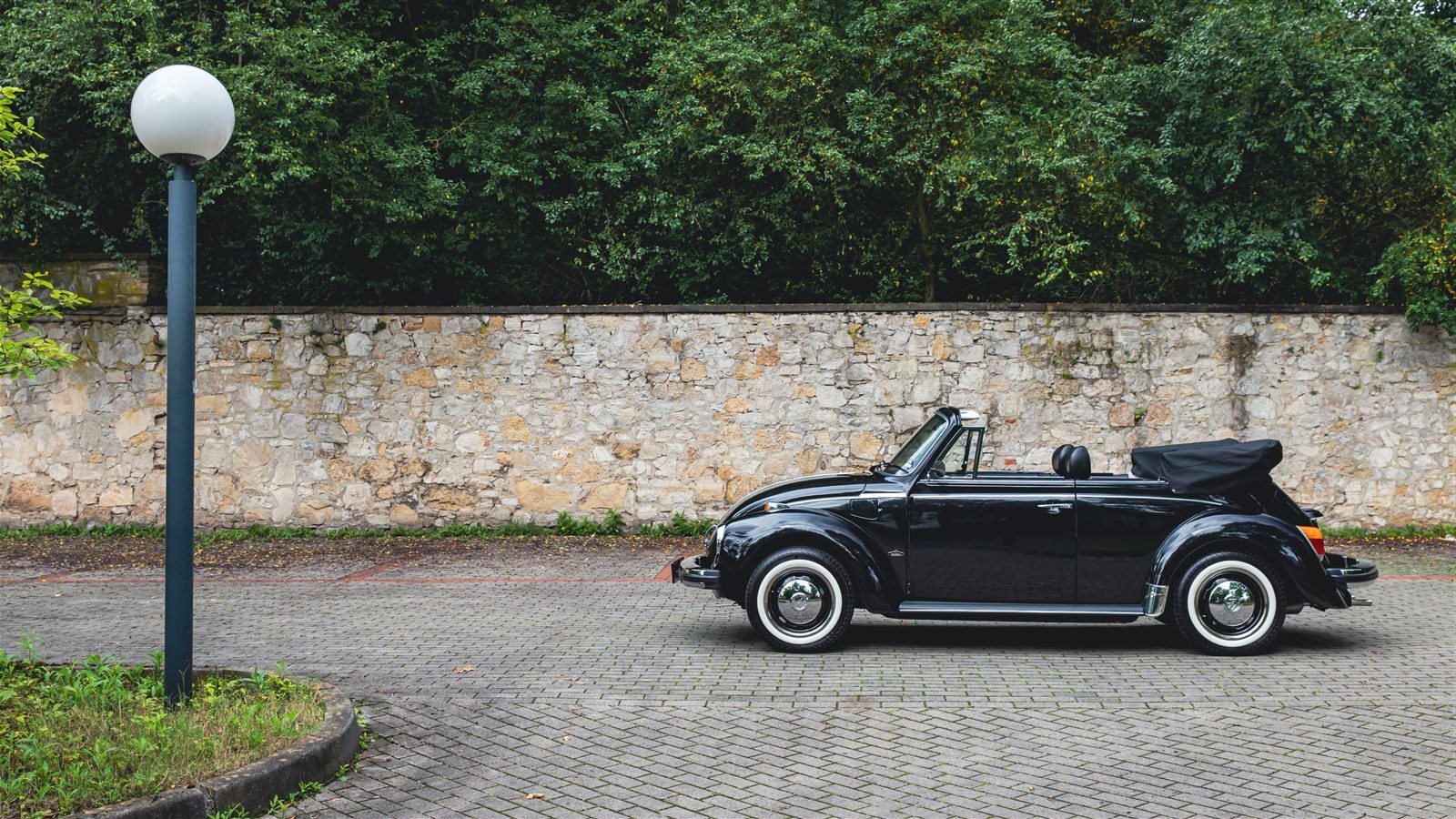 Volkswagen Beetle descapotable negro junto a un muro de piedra