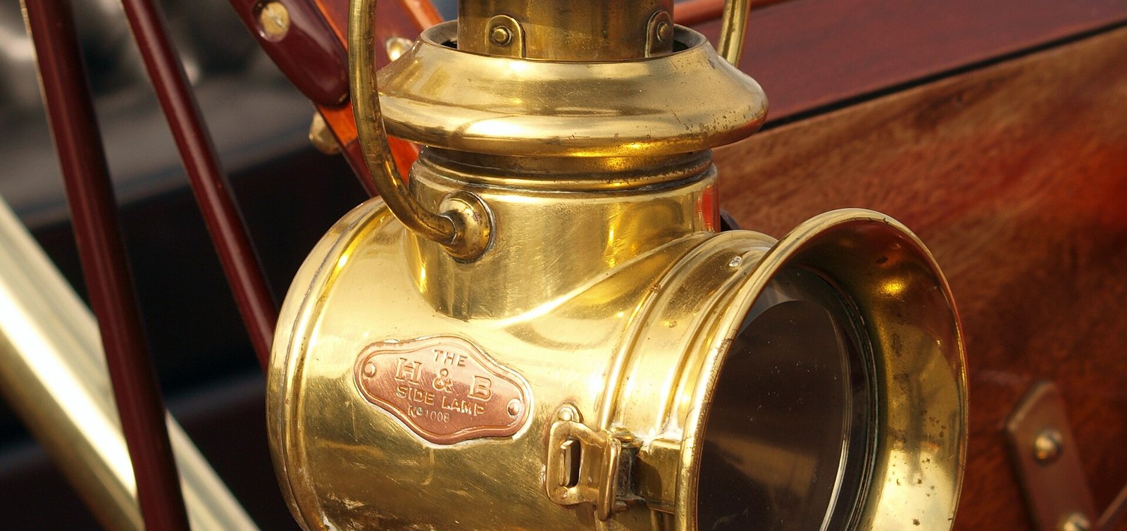 Farol de latón de un automóvil de 1910, con la carrocería de madera barnizada al fondo