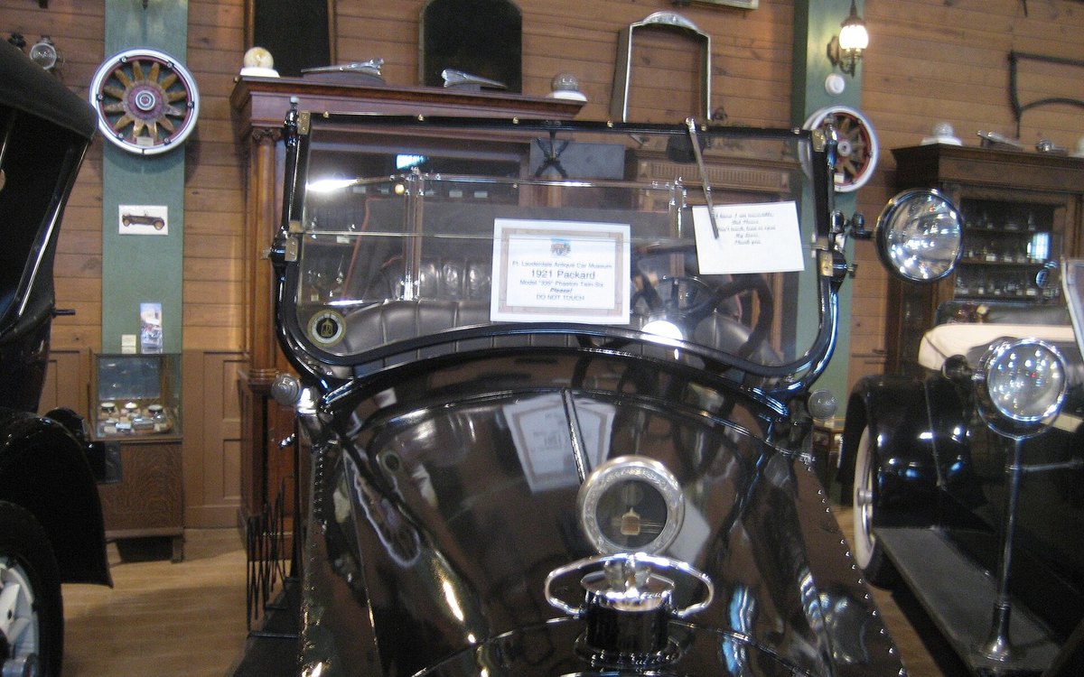 Frontal de un Packard de 1921 expuesto en un museo del automóvil, con el parabrisas plano, el tapón del radiador cromado y paneles de madera al fondo.