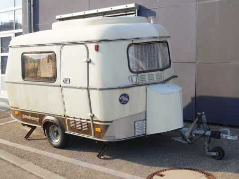 Caravana clásica Eriba Touring de color crema, con techo elevable y una sola rueda por lado, aparcada de perfil junto a una nave.