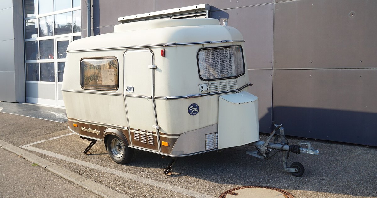Caravana clásica Eriba Touring de color crema, con techo elevable y una sola rueda por lado, aparcada de perfil junto a una nave.