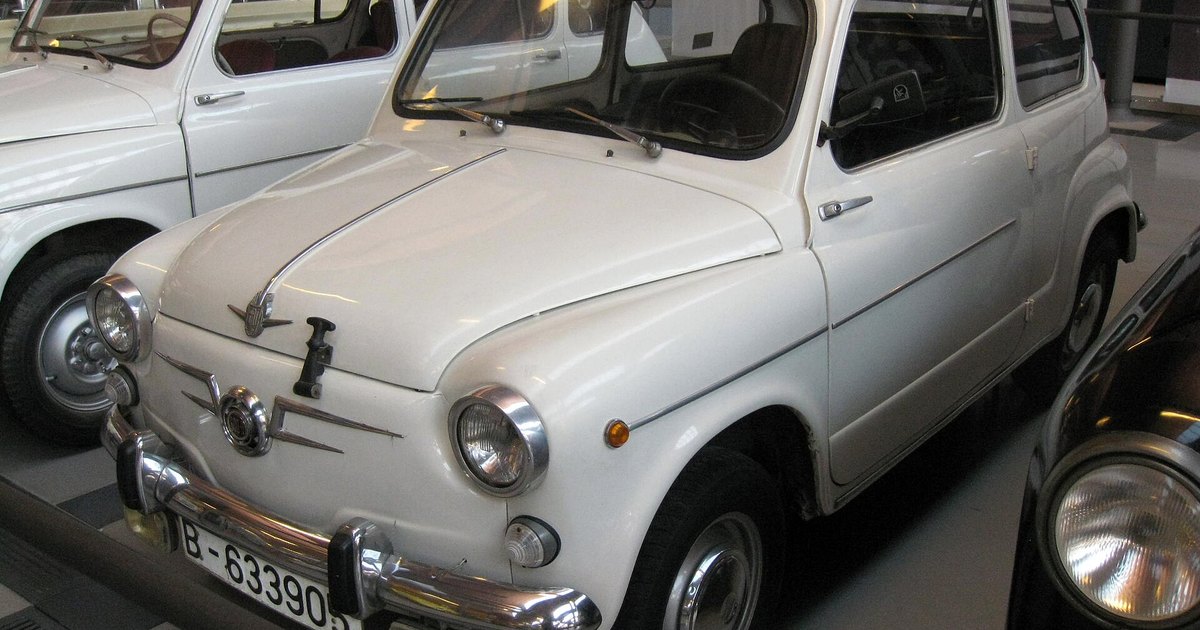 SEAT 600 blanco expuesto en un museo, visto en tres cuartos delantero, con otro 600 detrás.