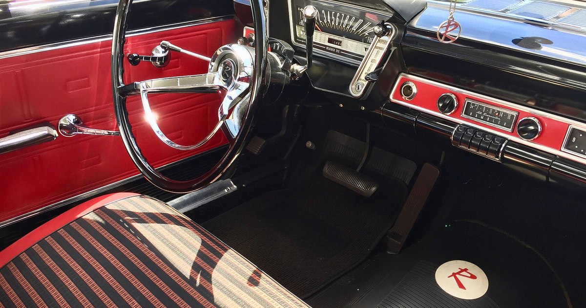Interior de un automóvil clásico de 1963: volante de dos radios, salpicadero con relojes cromados, tapicería roja y negra a rayas y radio de la época.