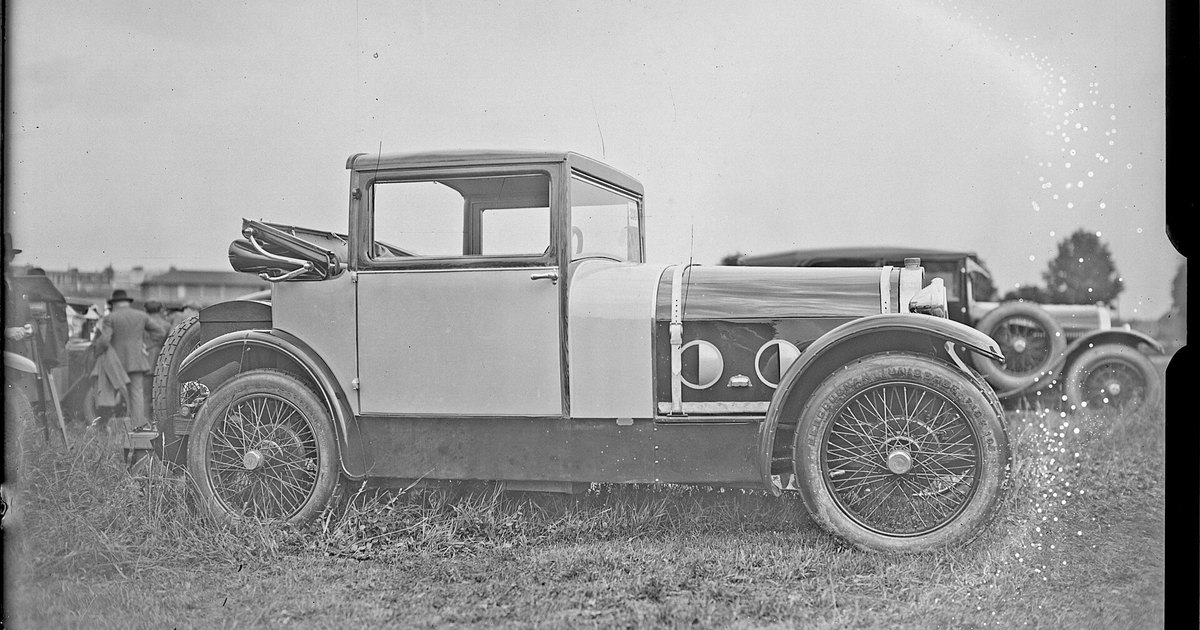 Coupé de dos plazas de 1926 fotografiado de perfil sobre la hierba, en un concurso de elegancia, con ruedas de radios y neumáticos de banda blanca.