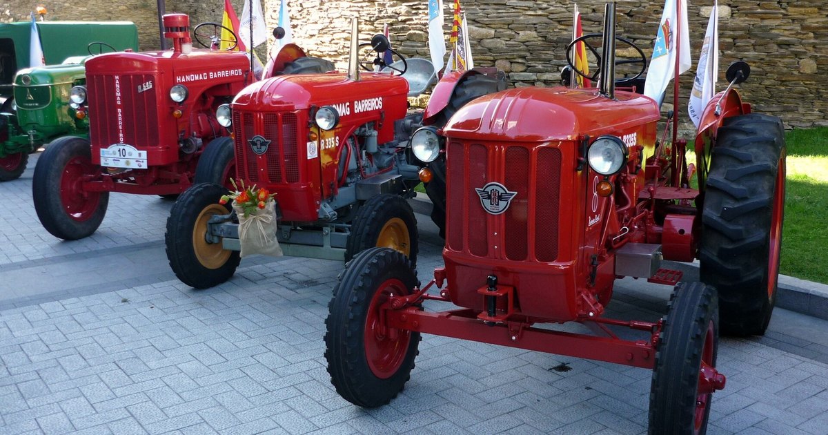 Tres tractores clásicos Hanomag Barreiros restaurados, pintados de rojo, alineados junto a una muralla de piedra en una concentración de maquinaria agrícola antigua.